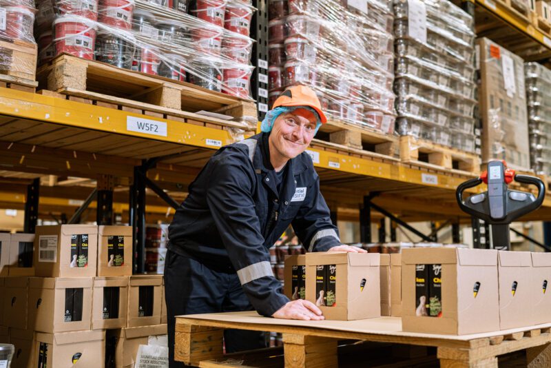 Essential Cuisine - behind the scenes 2 Warehouse team member smiling while handling boxes of Essential Cuisine Signature Chicken Stock Reduction