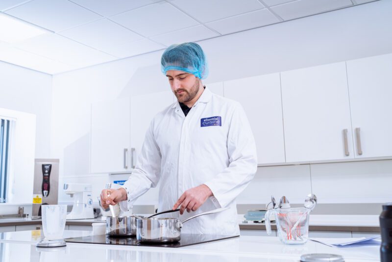 Essential Cuisine - behind the scenes 5 Chef in whites testing and stirring a recipe in Essential Cuisine's development kitchen