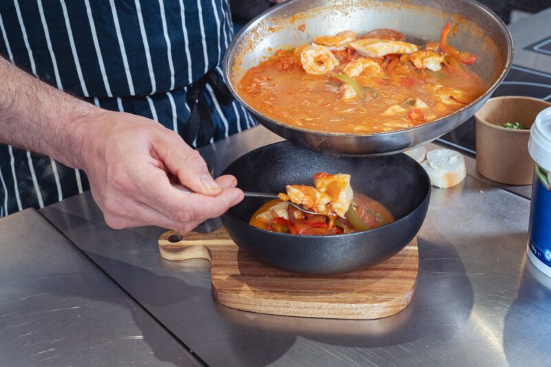 Essential Cuisine - behind the scenes 7 Chef spooning a seafood stew made with Essential Cuisine stock from pan into serving bowl