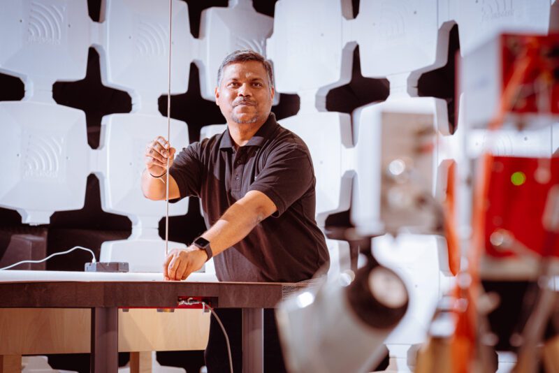 SGS technician positioning a thin antenna element at a test bench inside an RF semi-anechoic chamber lined with cross-shaped absorber panels