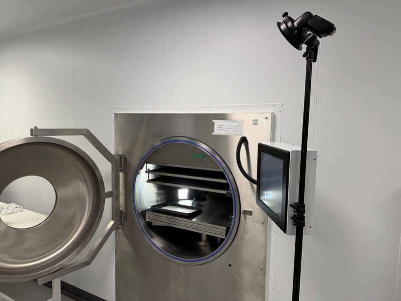 Shot Entirely In-Camera: One Freeze-Dryer Session Built Biofortuna's Exhibition Stand Hero Image 2 Open freeze-dryer chamber showing shelves, camera and tray inside, with an external monitor mounted beside the door for remote framing
