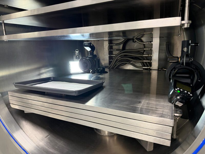 Shot Entirely In-Camera: One Freeze-Dryer Session Built Biofortuna's Exhibition Stand Hero Image 1 Close-up of a mirrorless camera, off-camera flash and remote trigger rigged beside an empty tray inside the freeze-dryer chamber