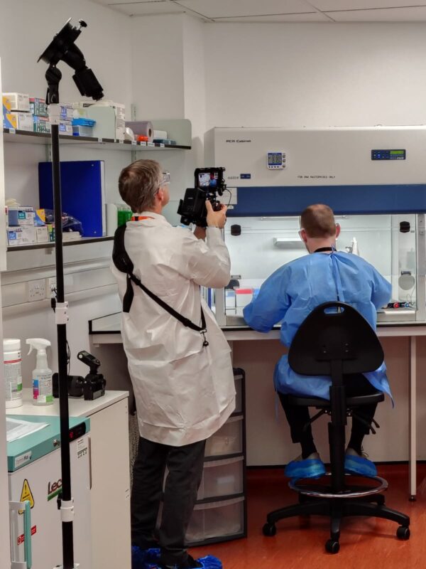 Growing a Commercial & Industrial Photography Business 8 Photographer in PPE filming a technician seated at a PCR cabinet using a camera mounted on a monopod with a monitor, during the SGS Vitrology Glasgow shoot.