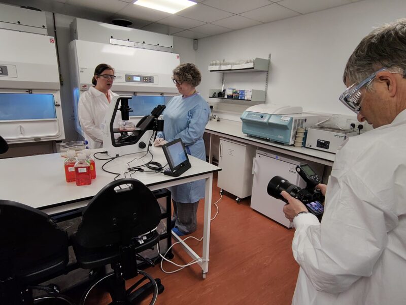 Photographing the People Behind SGS Vitrology's New Glasgow Lab 5 Photographer capturing two scientists talking beside a microscope and cell culture bottles, reviewing shots on his camera screen, during the SGS Vitrology Glasgow shoot.