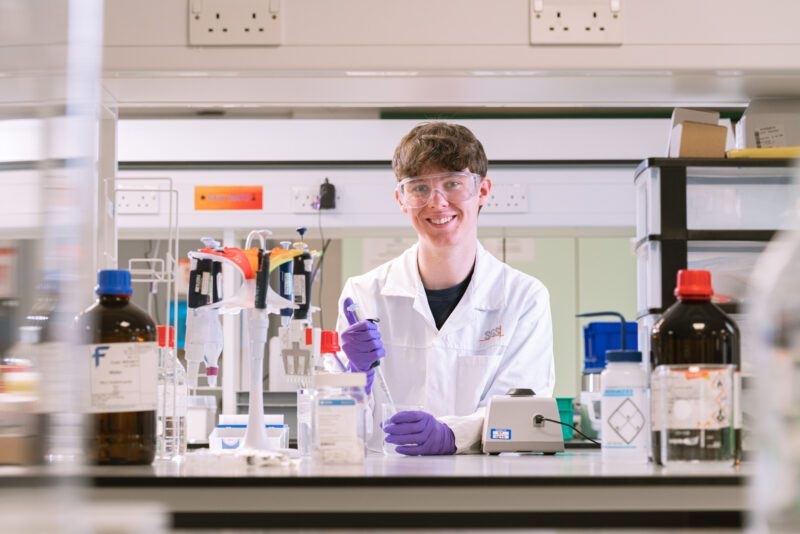 Photographing the People Behind SGS Vitrology's New Glasgow Lab 8 Young analyst in an SGS lab coat smiling at the camera while preparing a sample with a pipette in the Glasgow laboratory.