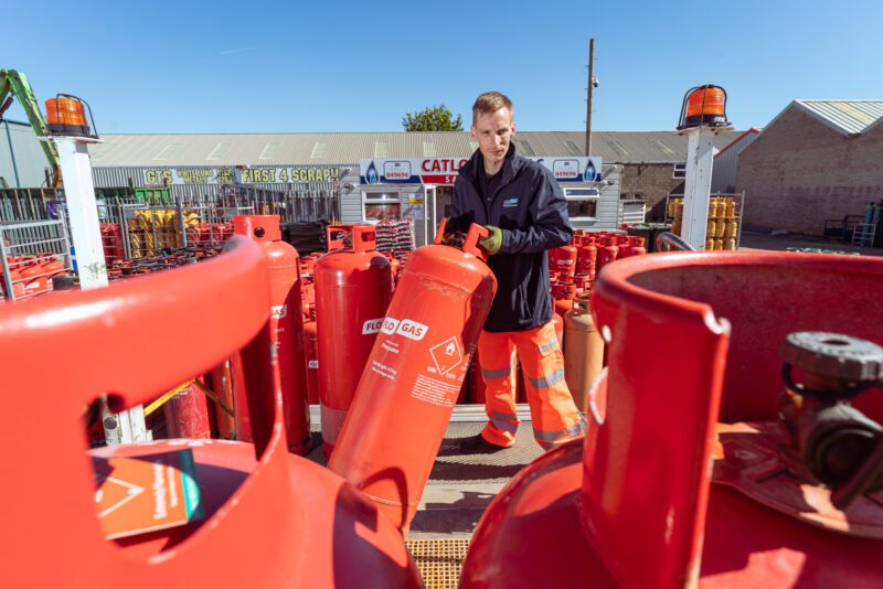 FloGas dealer team member wheeling a large orange propane cylinder through the yard at Catlow's, White Lund, Morecambe