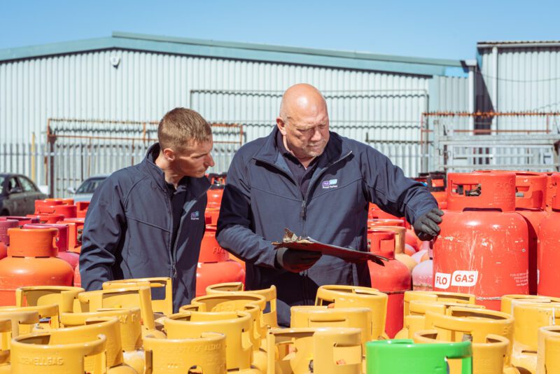 Two FloGas Proud Partner staff members inspecting yellow gas cylinders against a clipboard checklist in the yard
