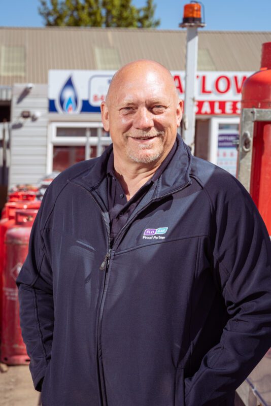 Smiling FloGas Proud Partner dealer team member standing in the yard with red gas cylinders behind him