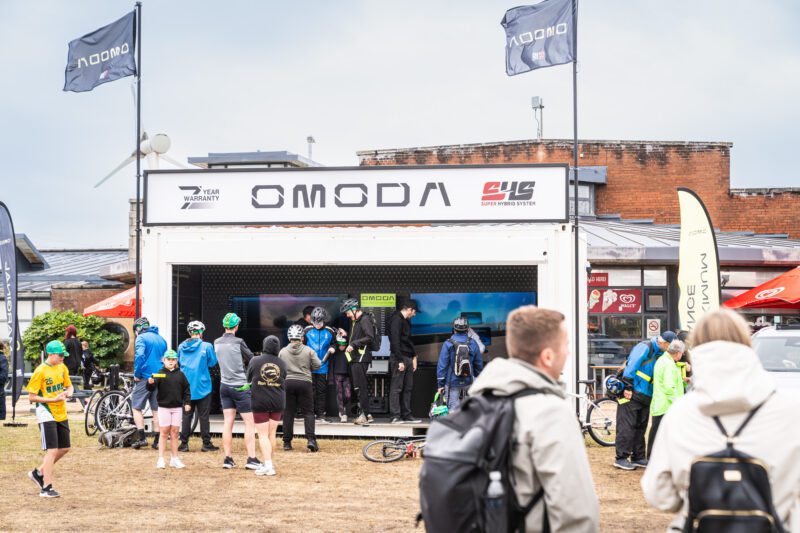 Shooting OMODA's Brand Activation at the Tour of Britain Women's, Blackpool 1 A crowd of visitors gathers around the OMODA branded pop-up unit at the Tour of Britain Women's Blackpool Event Village on an overcast day